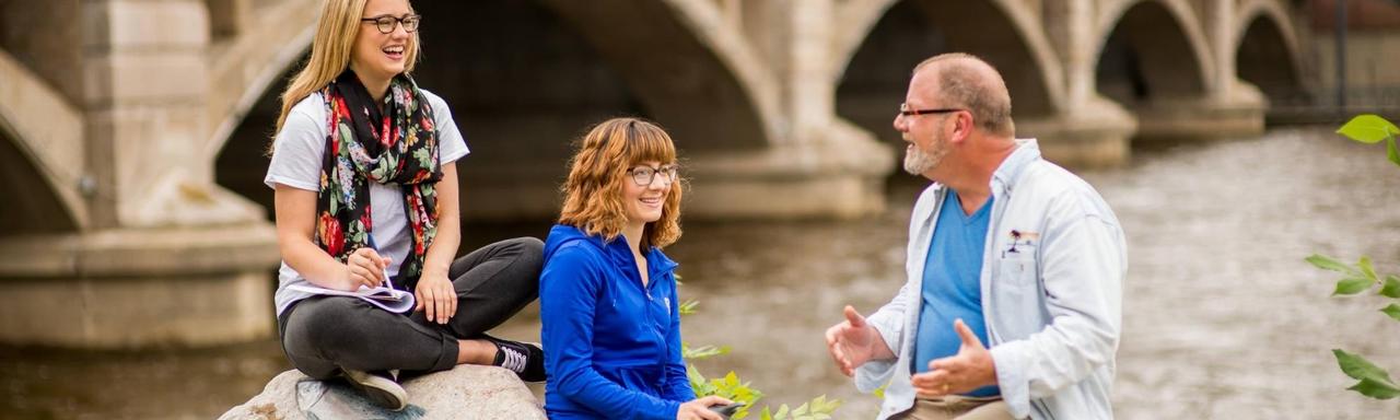 Two students talking with their professor by the Grand River